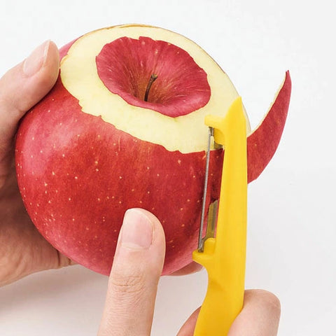 Hand holding a red apple with a yellow peeler cutting into it on a white background