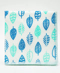 A square fabric napkin or small cloth with a repeating leaf pattern in shades of blue and mint green on a white background, photographed against a clean white studio backdrop.
