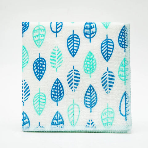 A square fabric napkin or small cloth with a repeating leaf pattern in shades of blue and mint green on a white background, photographed against a clean white studio backdrop.