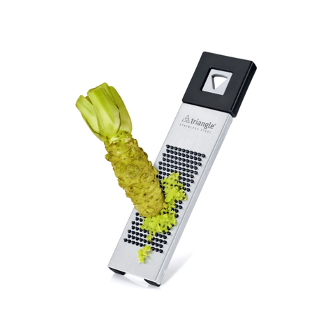 Triangle stainless steel vegetable grater with a black handle, shown grating fresh wasabi on a white background.