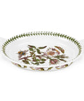 A white oval ceramic baking dish with side handles, decorated with a vintage botanical floral pattern featuring green leaves, pink flowers, and a bee, on a white background.