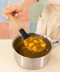 Person holding a wooden and silicone spoon with food over a pot of soup