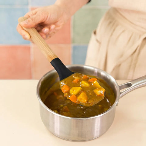 Person holding a wooden and silicone spoon with food over a pot of soup