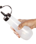 A hand holding a translucent white squeeze bottle with a black nozzle and curved spout against a plain white background.
