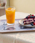 Glass of orange juice and slice of berry cheesecake on a tray with swan design.