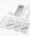 A white plastic mandoline slicer set with multiple interchangeable blade plates and a clear plastic cover, arranged on a clean white background.