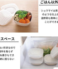 White square plastic bento containers with matching lids, shown on a light wood surface and inside a refrigerator. One container is open with vegetables inside, and a hand is lifting a lid to demonstrate storage space.