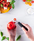 Person using a tomato corer on a red tomato with a white background featuring tomatoes and basil.