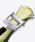Zucchini being sliced with a silver vegetable peeler on a white background