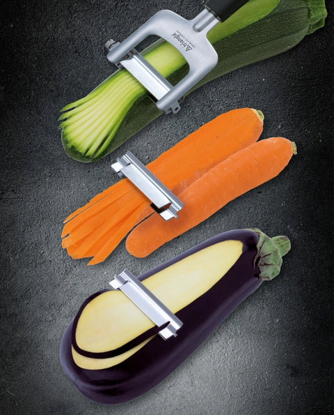 Vegetable peeler with zucchini, carrots, and eggplant on a dark background