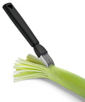 A kitchen utensil with a matte black handle and silver metal tines, shown slicing a green leek on a clean white background.