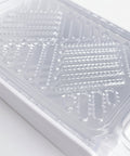 A close-up of a clear plastic grater with a white base, showing the textured grating surfaces and handle attachment, set against a white background.