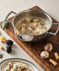 Stainless steel pot with mushroom pasta dish on a wooden board