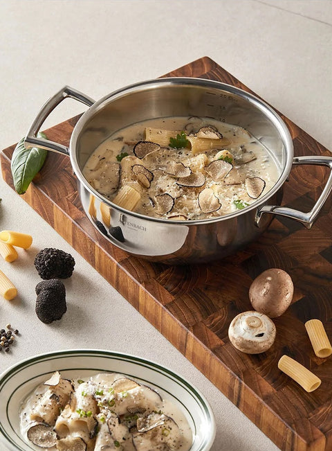 Stainless steel pot with mushroom pasta dish on a wooden board