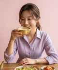 Woman drinking from a gold cup with a pink background
