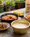Assorted Korean dishes on a wooden table with a bottle of soy sauce in the background.