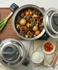 Stew in a pot with vegetables and a small plate of food on a table.