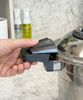A hand unlocking a pressure cooker pot handle with a kitchen counter in the background