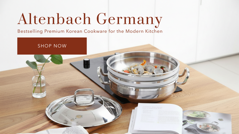 A stainless steel multi-tier steamer pot set on a wooden table, with its matching lid placed beside it. An open cookbook and a small vase with green leaves are also visible on the table. The title says 'Altenbach Germany' with a 'SHOP NOW' button underneath.