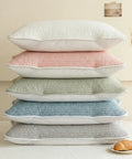 Stack of five textured pillows in white, pink, green, blue, and gray on a light surface.