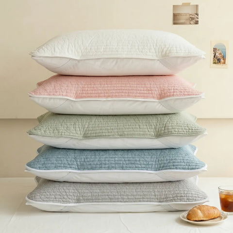 Stack of five textured pillows in white, pink, green, blue, and gray on a light surface.