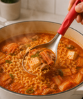 Serving of ramen soup with a spoon lifting noodles out of a pot.