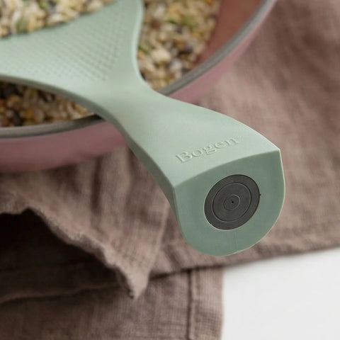 Close-up of a green rice spatula with 'Bogen' branding, held over a container of food.