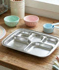 Stainless steel divided tray on a wooden table with colorful bowls and measuring cups in the background.