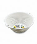A white plastic colander basket with vertical slits and a small handle, shown on a neutral gray background. A circular paper label is visible inside the basket.