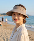 Woman wearing a beige visor on a beach with ocean and sky in the background