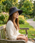 Woman sitting on a bench in a park wearing a wide-brimmed hat.