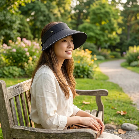 Woman sitting on a bench in a park wearing a wide-brimmed hat.