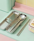 Metal lunch box with cutlery set on a pastel green surface