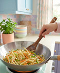 Person cooking stir-fry in a wok with vegetables in a kitchen.