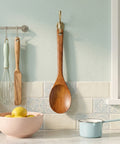 Wooden spoon hanging on a hook with kitchen utensils and a bowl on a countertop.