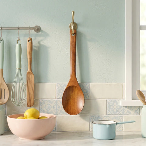 Wooden spoon hanging on a hook with kitchen utensils and a bowl on a countertop.