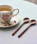 Teacup with floral design on a saucer, accompanied by two wooden spoons on a light surface.