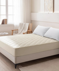 Beige mattress cover on a bed in a bedroom setting with pillows and a chair.