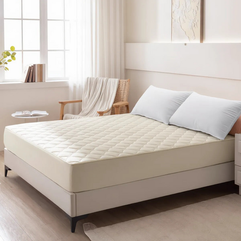 Beige mattress cover on a bed in a bedroom setting with pillows and a chair.