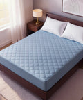 Blue mattress pad on a bed in a bedroom setting with a lamp and window.