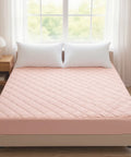 Pink mattress cover on a bed with white pillows in a bright room.