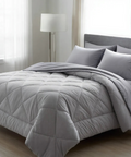 Gray comforter on a bed in a bedroom setting with a lamp and window.