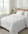 White comforter on a bed in a bright bedroom with large windows.