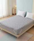 Gray mattress protector on a bed in a bedroom setting with light decor