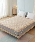 Bed with beige mattress cover and white pillows in a bedroom setting.
