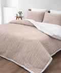 Beige quilted comforter and pillows on a bed in a bedroom setting.