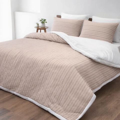 Beige quilted comforter and pillows on a bed in a bedroom setting.