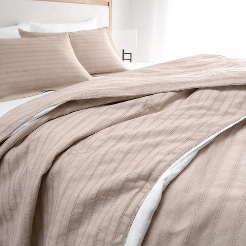 Beige striped bedding set on a bed with white pillows.
