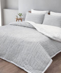 Gray textured comforter on a bed with white pillows in a bedroom setting.