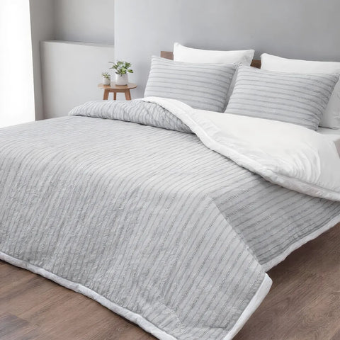 Gray textured comforter on a bed with white pillows in a bedroom setting.